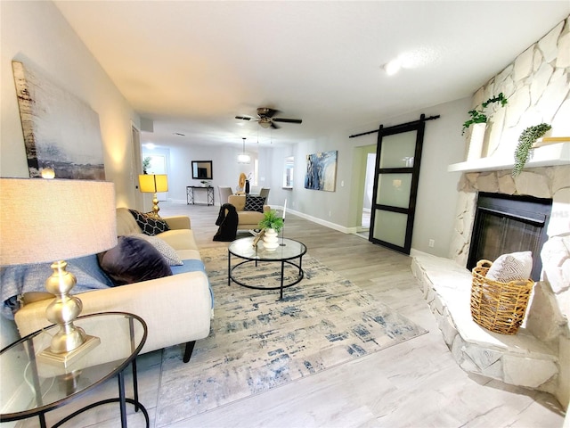 living room featuring ceiling fan, a barn door, a fireplace, wood finished floors, and baseboards