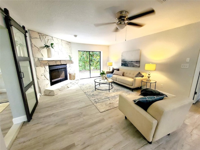 living room with a textured ceiling, a stone fireplace, wood finished floors, a ceiling fan, and baseboards