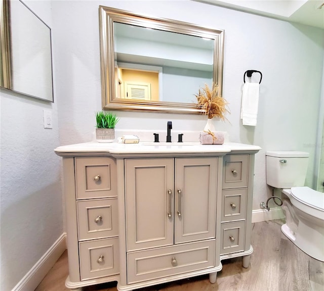 bathroom with wood finished floors, vanity, toilet, and baseboards