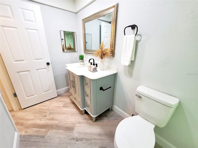 half bathroom with baseboards, vanity, toilet, and wood finished floors