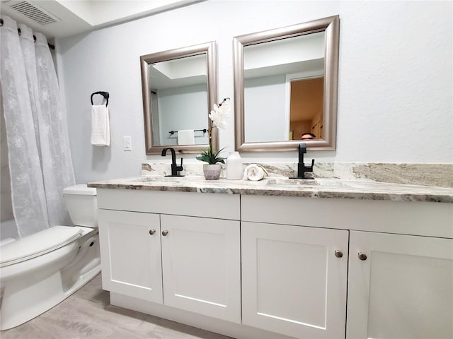 bathroom featuring double vanity, visible vents, toilet, a sink, and wood finished floors