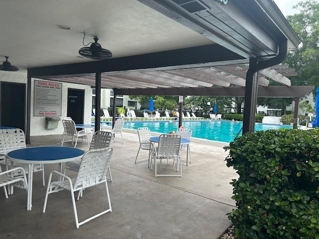 view of patio featuring a community pool, ceiling fan, and a pergola