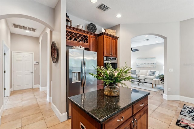 kitchen featuring light tile patterned flooring, stainless steel appliances, a center island, and dark stone countertops