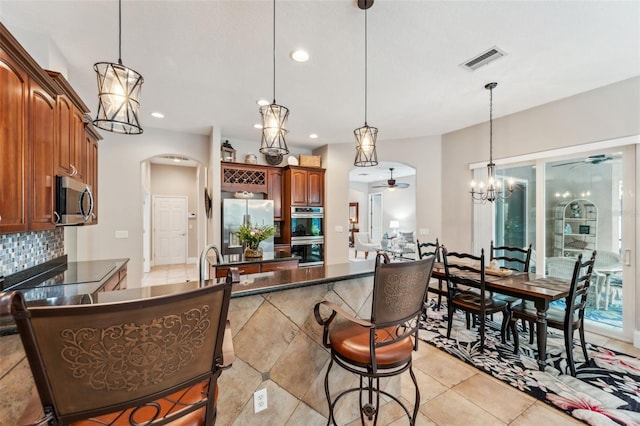 kitchen featuring appliances with stainless steel finishes, a breakfast bar, ceiling fan with notable chandelier, pendant lighting, and sink