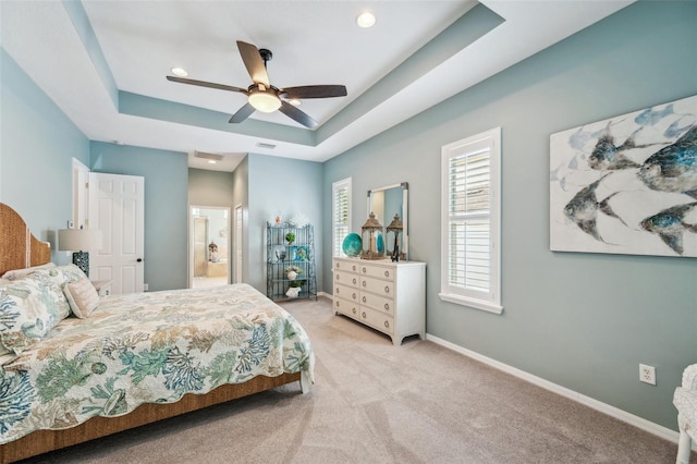 bedroom with a raised ceiling, connected bathroom, light colored carpet, and ceiling fan