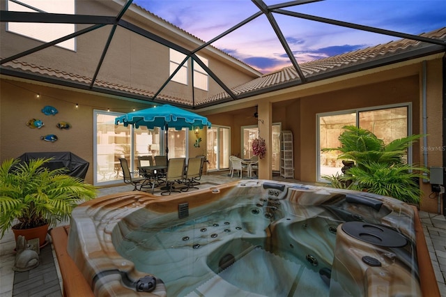 pool at dusk with a hot tub, a patio, and a lanai