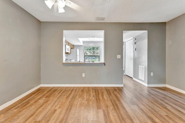 spare room featuring ceiling fan, light hardwood / wood-style flooring, and a textured ceiling