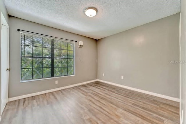 empty room with a textured ceiling and light hardwood / wood-style flooring