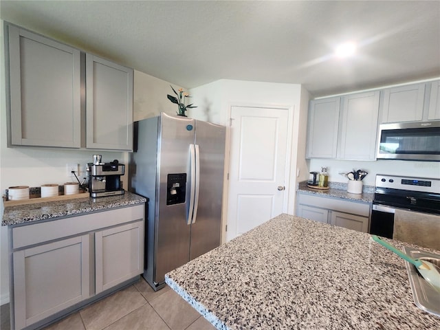 kitchen with light stone countertops, stainless steel appliances, gray cabinets, and light tile patterned floors