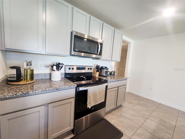 kitchen with light tile patterned flooring, appliances with stainless steel finishes, and light stone counters