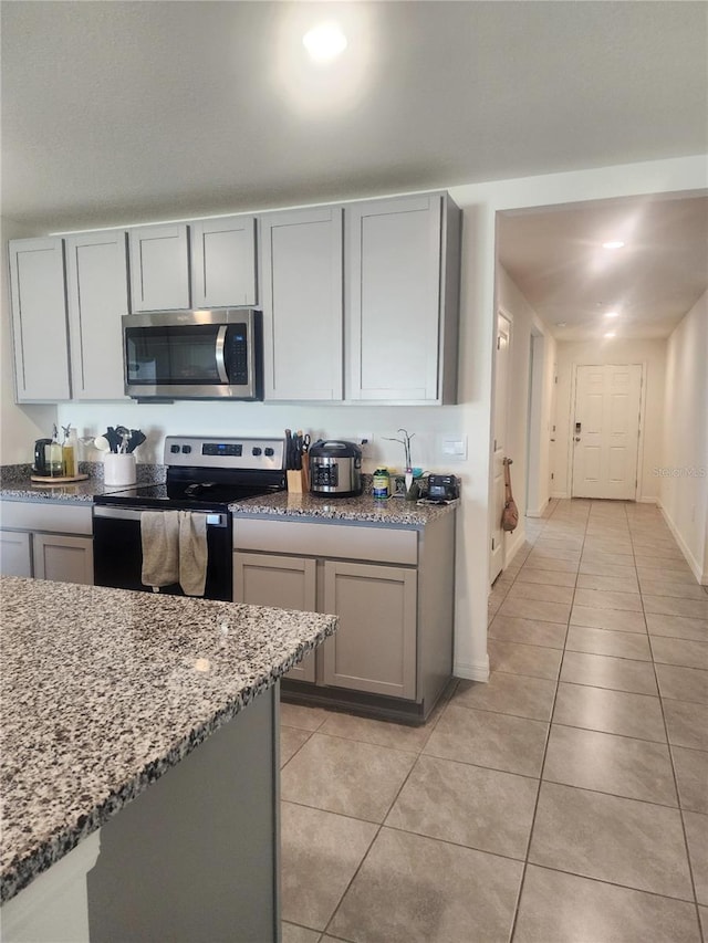 kitchen featuring light stone countertops, stainless steel appliances, gray cabinets, and light tile patterned floors