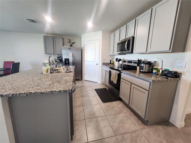 kitchen with light tile patterned flooring, gray cabinets, appliances with stainless steel finishes, stone countertops, and sink