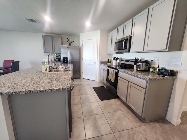 kitchen featuring a center island with sink, stainless steel appliances, visible vents, gray cabinetry, and a sink