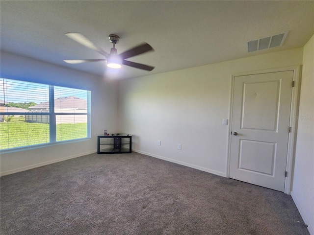 empty room with baseboards, visible vents, dark carpet, and a ceiling fan