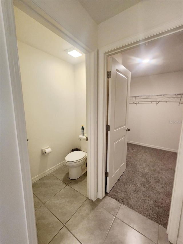 bathroom featuring a walk in closet, tile patterned flooring, toilet, and baseboards