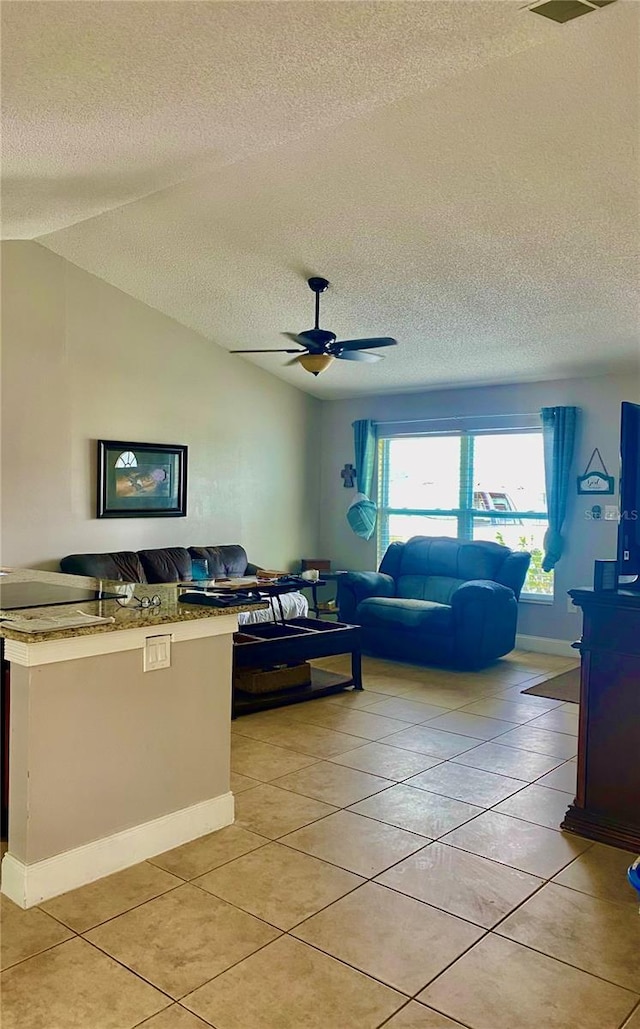 living area featuring lofted ceiling, ceiling fan, a textured ceiling, and light tile patterned flooring