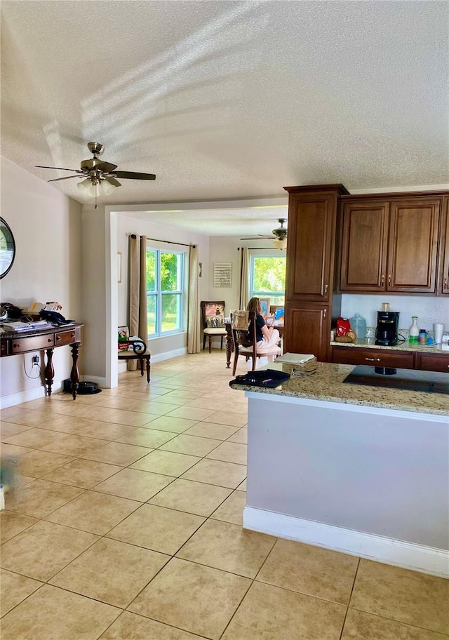 kitchen featuring ceiling fan, light tile patterned floors, a textured ceiling, and light stone counters