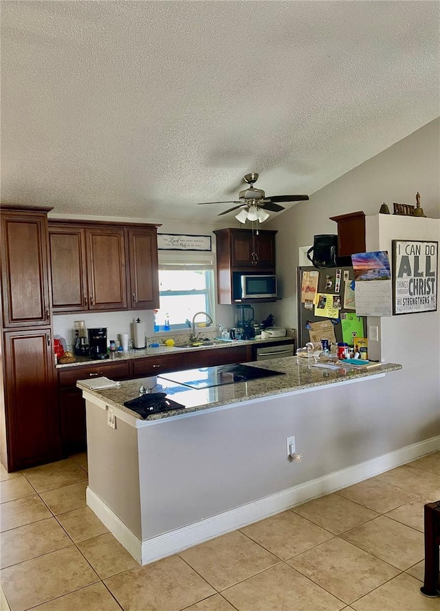 kitchen featuring a peninsula, stainless steel appliances, a sink, and light tile patterned flooring