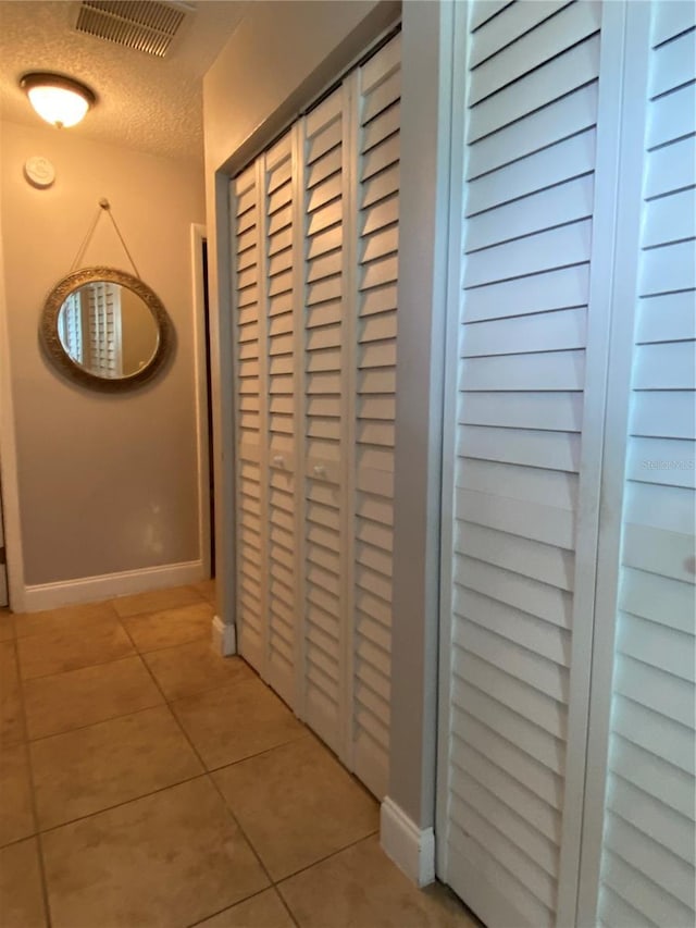 hallway with baseboards, light tile patterned flooring, visible vents, and a textured ceiling