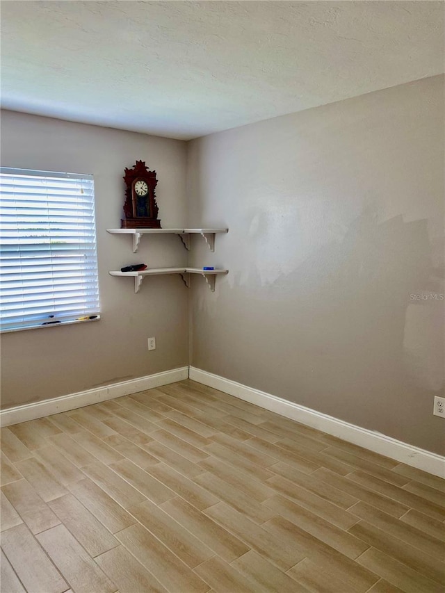 spare room featuring a textured ceiling, light wood finished floors, and baseboards