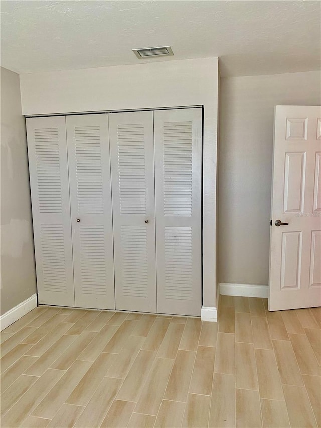 unfurnished bedroom featuring wood tiled floor, a closet, visible vents, and baseboards