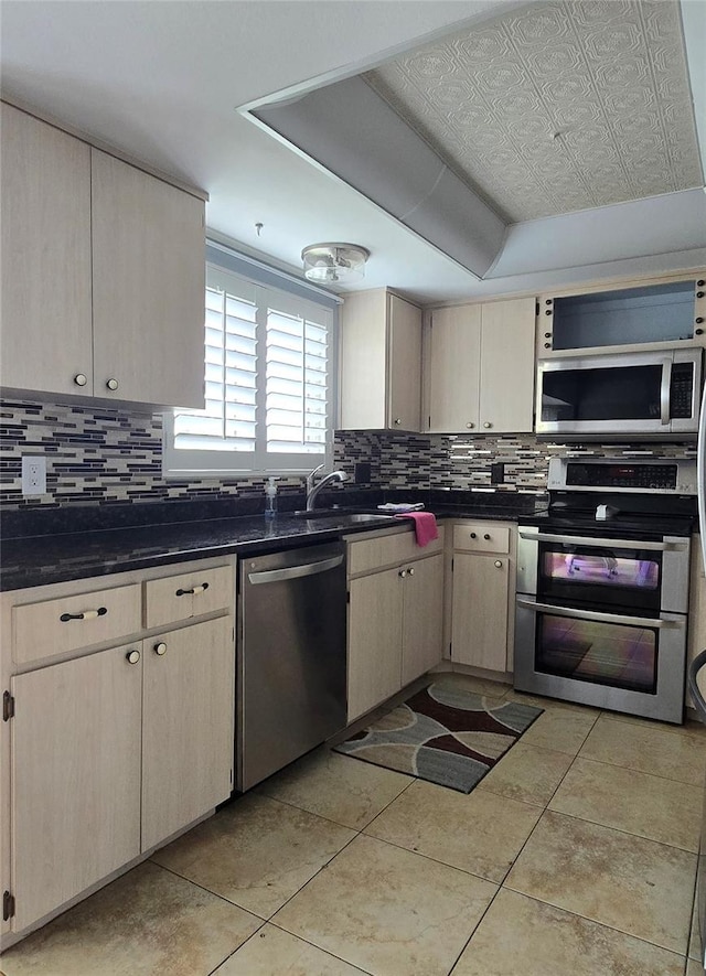 kitchen featuring light tile patterned flooring, light brown cabinets, appliances with stainless steel finishes, decorative backsplash, and sink