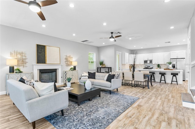 living room with a glass covered fireplace, ceiling fan, and light wood finished floors