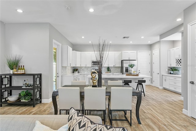 kitchen with light wood finished floors, an island with sink, appliances with stainless steel finishes, a breakfast bar, and light countertops