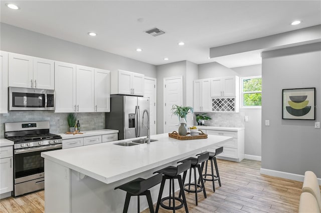 kitchen featuring visible vents, appliances with stainless steel finishes, an island with sink, light wood-type flooring, and a kitchen breakfast bar