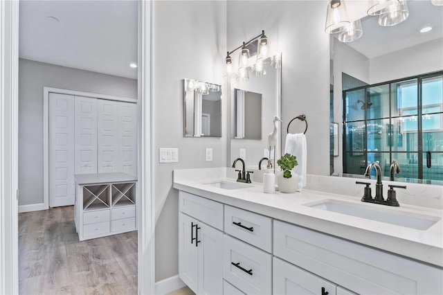 bathroom featuring double vanity, a shower stall, a sink, and wood finished floors