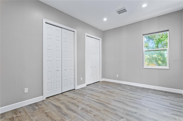 unfurnished bedroom with baseboards, visible vents, multiple closets, and wood finished floors