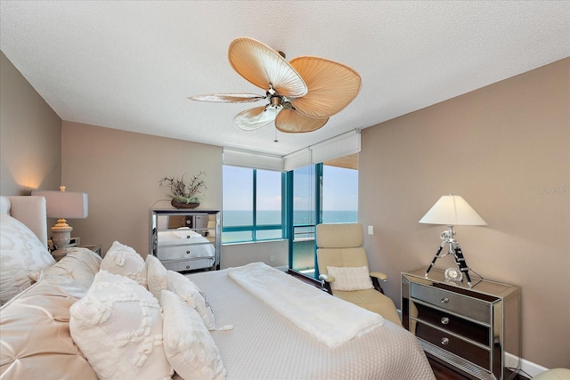 bedroom with a water view, a textured ceiling, ceiling fan, and a wall of windows