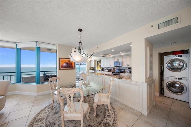 tiled dining area featuring a water view, a textured ceiling, stacked washer / drying machine, and a chandelier