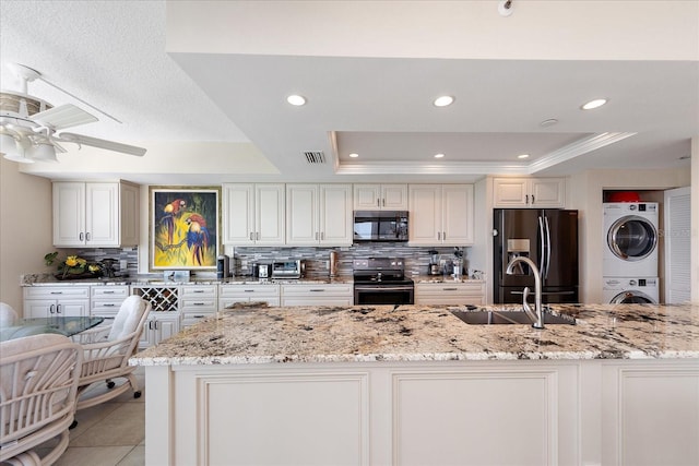 kitchen with black appliances, estacked washer and dryer, a raised ceiling, decorative backsplash, and a ceiling fan
