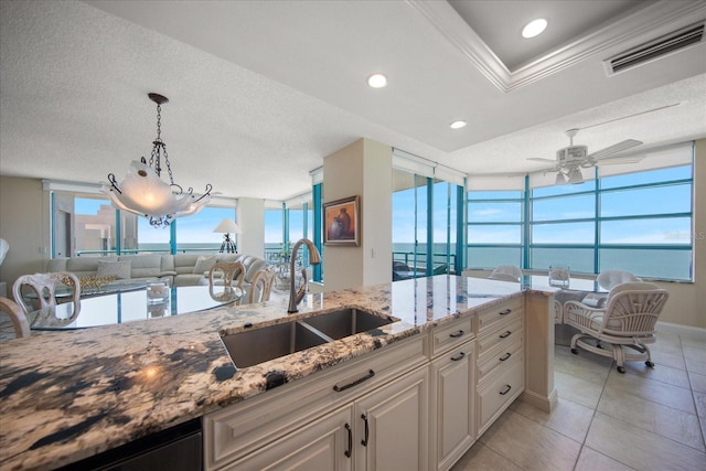 kitchen with a sink, open floor plan, light stone counters, hanging light fixtures, and ceiling fan