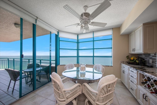 dining room featuring light tile patterned flooring, a textured ceiling, ceiling fan, and a water view