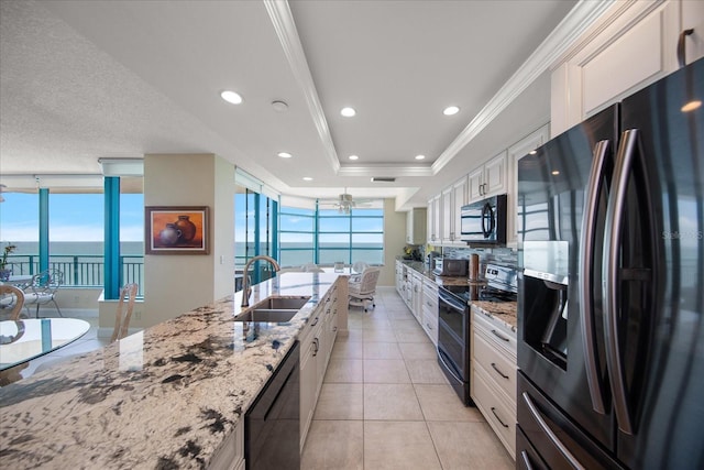kitchen featuring black appliances, a sink, white cabinetry, a water view, and ornamental molding