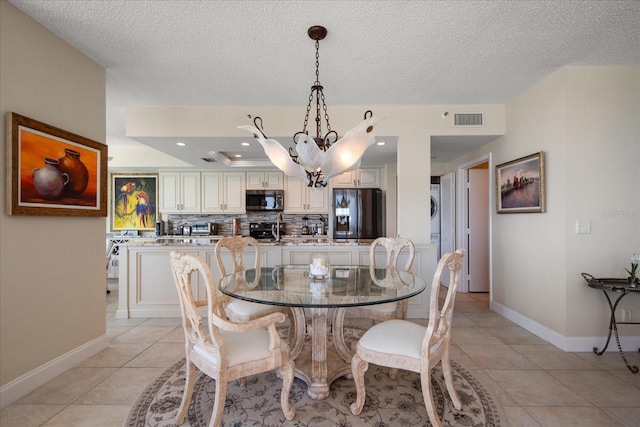 dining room with stacked washer / dryer, a chandelier, baseboards, a textured ceiling, and light tile patterned flooring