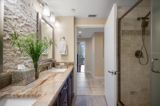 bathroom featuring a shower stall, double vanity, and baseboards