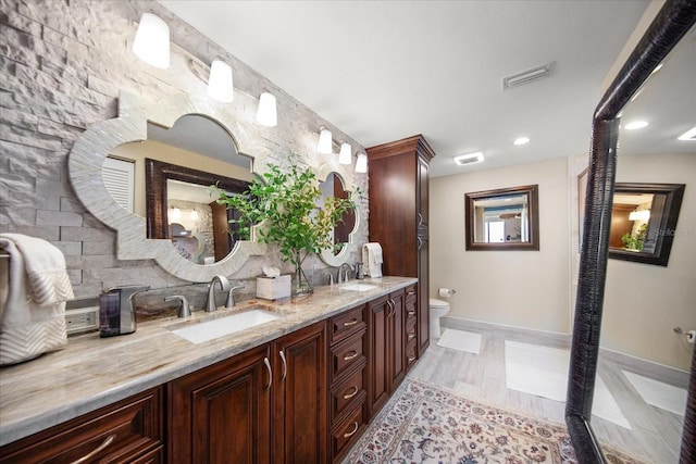 bathroom with toilet, baseboards, double vanity, and recessed lighting
