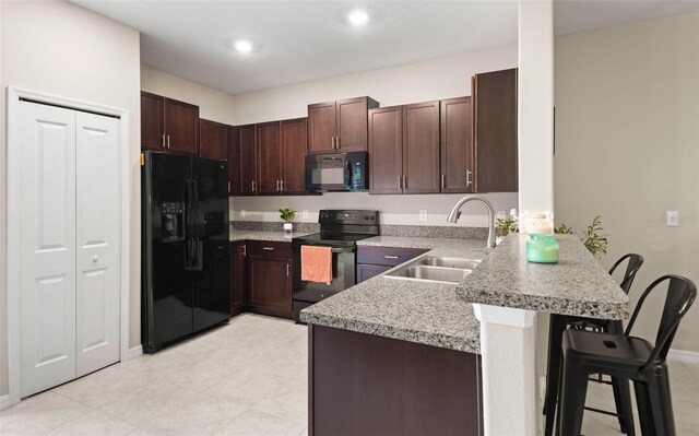 kitchen with black appliances, dark brown cabinets, a kitchen bar, sink, and kitchen peninsula