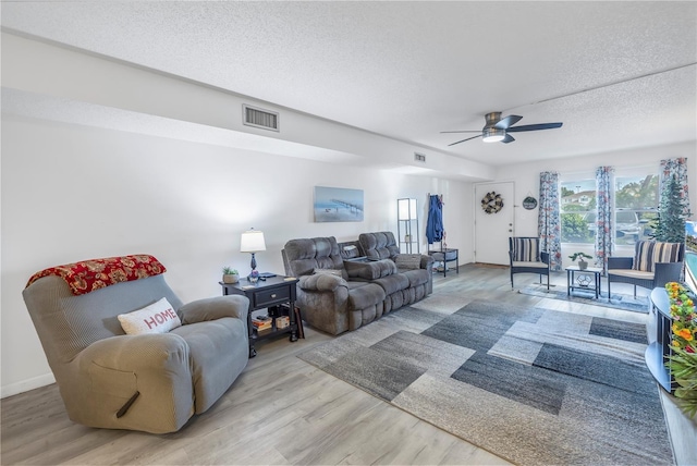 living room with ceiling fan, a textured ceiling, and light hardwood / wood-style floors