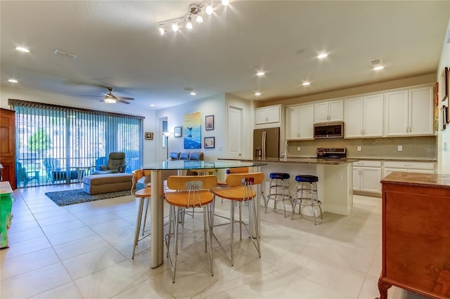 kitchen featuring a breakfast bar, white cabinetry, appliances with stainless steel finishes, a kitchen island with sink, and backsplash