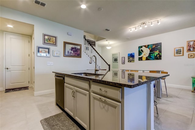 kitchen with sink, gray cabinets, a breakfast bar, dark stone countertops, and an island with sink