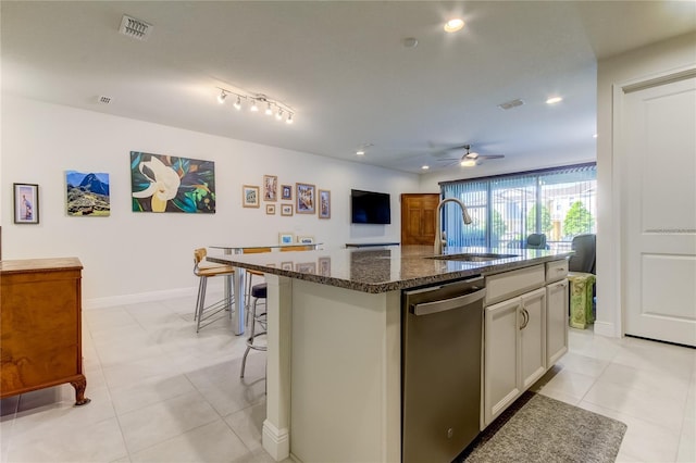 kitchen featuring a kitchen bar, sink, dishwasher, dark stone counters, and a kitchen island with sink