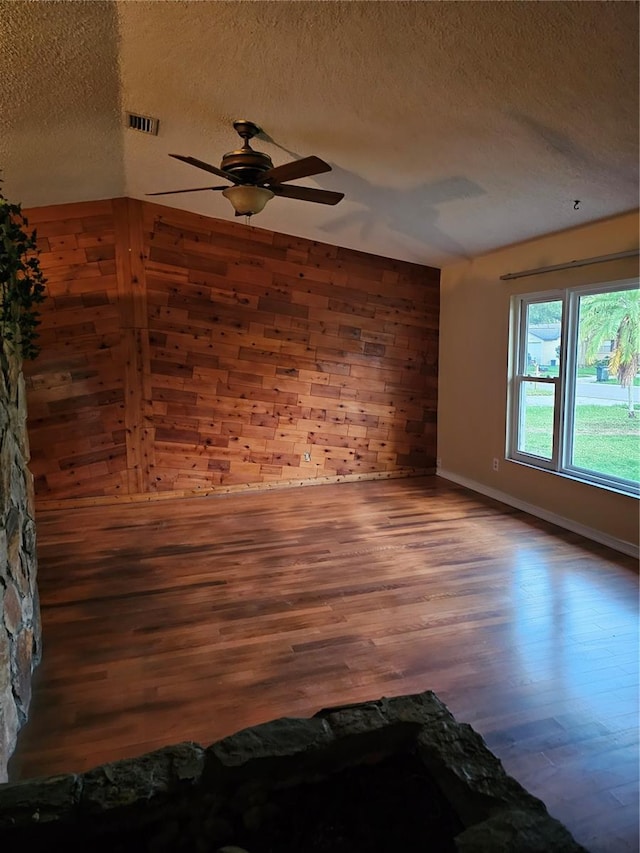 spare room featuring hardwood / wood-style flooring, ceiling fan, a textured ceiling, and wooden walls