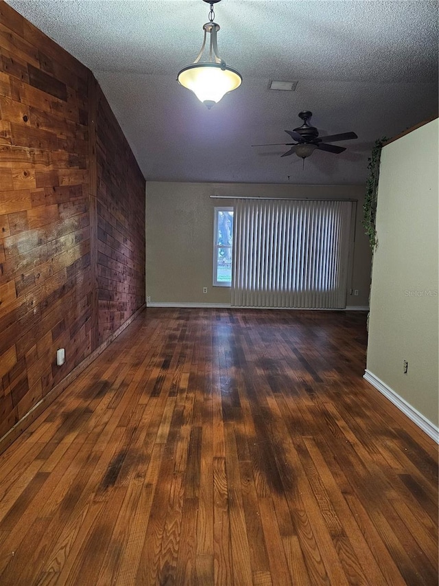 spare room with ceiling fan, wooden walls, a textured ceiling, and dark hardwood / wood-style flooring