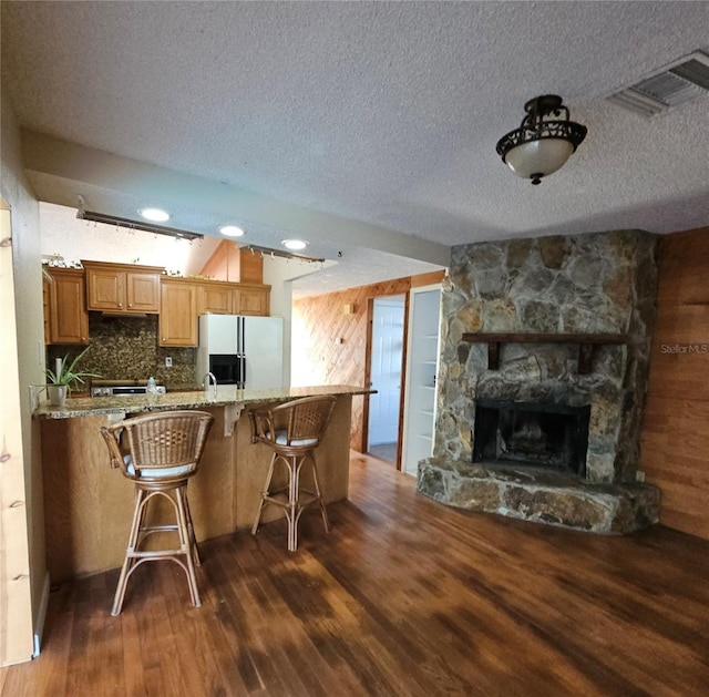 kitchen featuring dark wood-type flooring, a kitchen breakfast bar, fridge with ice dispenser, light stone counters, and wood walls