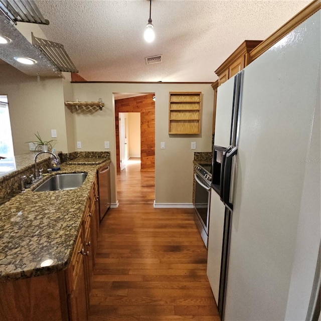 kitchen with dark wood-type flooring, sink, dark stone countertops, appliances with stainless steel finishes, and kitchen peninsula