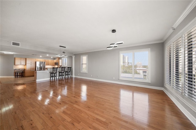 unfurnished living room featuring light wood finished floors, baseboards, visible vents, and crown molding